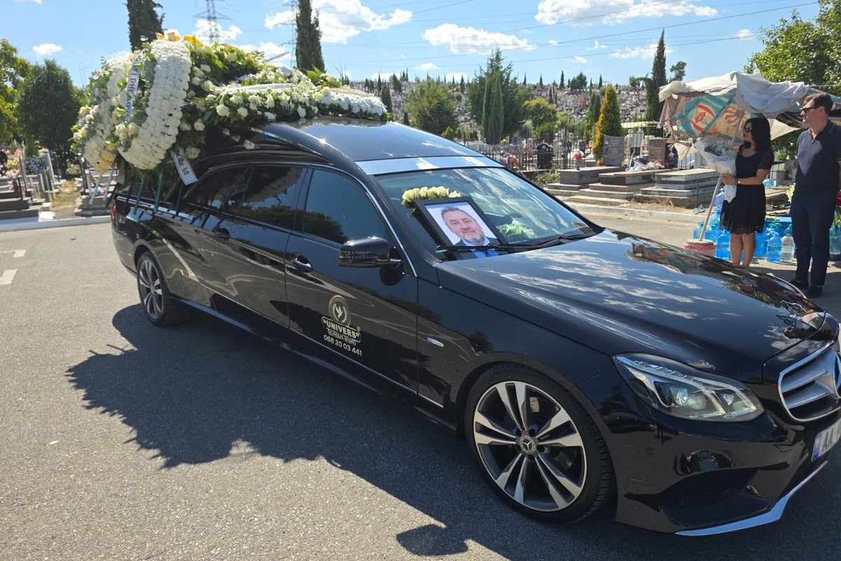 Makina mortore e Univers Funeral Home me kurora lulesh të bardha dhe fotografia e Prof. Skerdi Priftit, gjatë ceremonisë së fundit.
