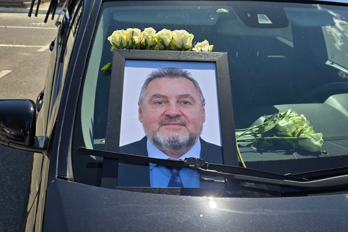 Fotografia e Prof. Skerdi Priftit e vendosur mbi makinën mortore, e rrethuar me trëndafila të bardhë.